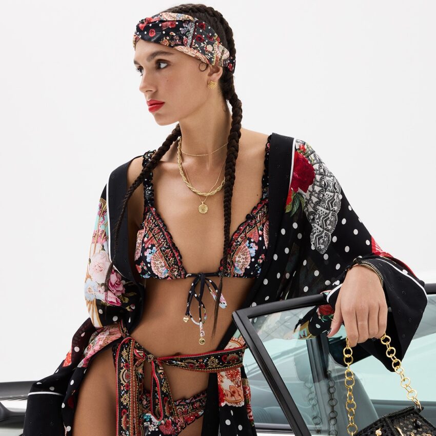Model in floral swimwear beside a convertible.
