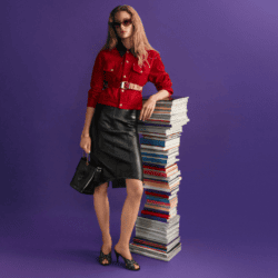 model wearing Versace red jacket and black skirt leaning on stack of books