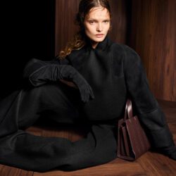 Model seated wearing Max Mara black coat with black turtleneck and trousers