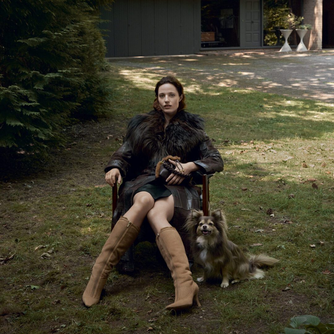 Model sitting wearing Jimmy Choo black coat and tan boots with dog
